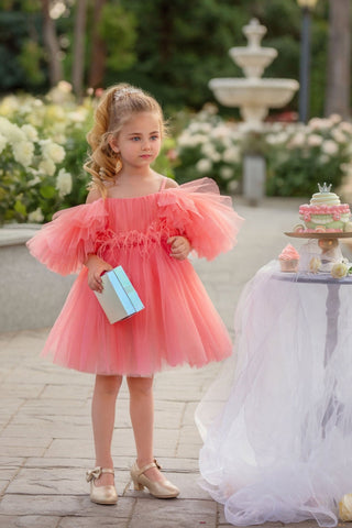 Young girl in a pink dress standing outdoors with a fountain and flowers in the background. Perfect faeella dress for photoshoots and portraits.