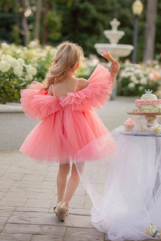 Young girl in a pink dress standing outdoors with a fountain and flowers in the background. Perfect faeella dress for photoshoots and portraits.