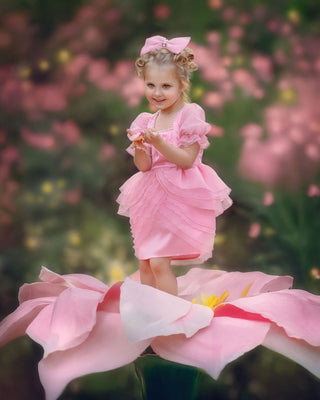 Girl standing on pink flower wearing faeella blush pink ruffle dress with puff sleeves perfect for holiday photoshoot