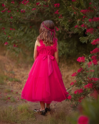 Young girl in a pink dress standing outdoors with flowers in the background. Faeella Rosy Enchantment Fairy Dress is perfect for portraits and holiday photoshoots.