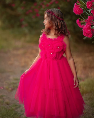 Young girl in a pink dress standing outdoors with flowers in the background. Faeella Rosy Enchantment Fairy Dress is perfect for portraits and holiday photoshoots.