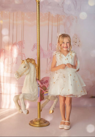 Girl in white star embroidered tulle dress by carousel in Faeella, perfect for holiday shoot, flower girl and weddings