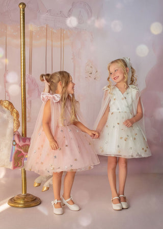 Girl in white star embroidered tulle dress with pearl details by carousel in Faeella, perfect for holiday shoot, flower girl and weddings
