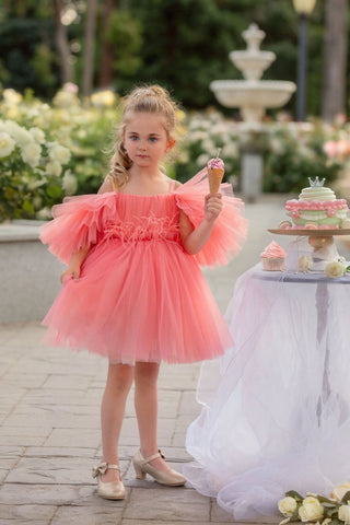 Young girl in a pink dress standing outdoors with a fountain and flowers in the background. Perfect faeella dress for photoshoots and portraits.
