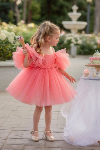 Young girl in a pink dress standing outdoors with a fountain and flowers in the background. Perfect faeella dress for photoshoots and portraits.