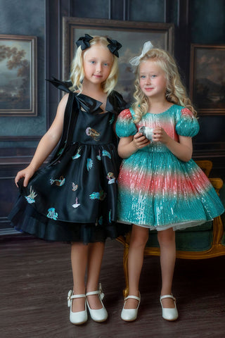 Two young girls in faeella party dresses standing in a room with paintings on the wall.