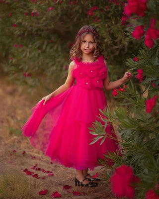 Young girl in a pink dress standing outdoors with flowers in the background. Faeella Rosy Enchantment Fairy Dress is perfect for portraits and holiday photoshoots.