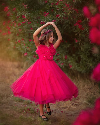Young girl in a pink dress standing outdoors with flowers in the background. Faeella Rosy Enchantment Fairy Dress is perfect for portraits and holiday photoshoots.