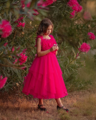 Young girl in a pink dress standing outdoors with flowers in the background. Faeella Rosy Enchantment Fairy Dress is perfect for portraits and holiday photoshoots.