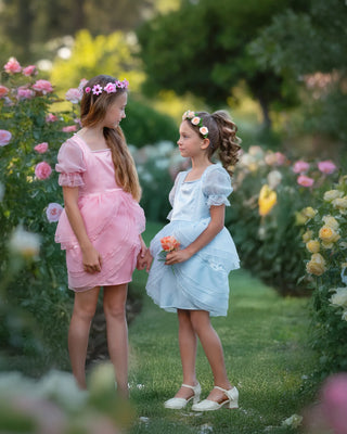 Girls in a rose garden wearing Faeella petal ruffle dresses, light blue Sky Petal Princess dress on the right